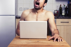 Young naked man watching pornography in his kitchen